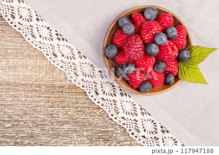 Plate with raspberries and blueberries on the wooden table with laced cloth. 117947188