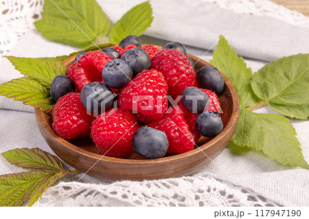 Plate with raspberries and blueberries on the wooden table with laced cloth. 117947190