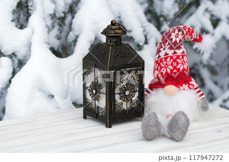 Toy gnome with red hat and lantern in the winter forest. 117947272