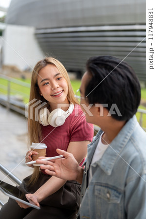 A smart Asian male college student is explaining a lesson on a digital tablet to his female friend. A smart Asian male college student is explaining a lesson on a digital tablet to his female friend. 117948831