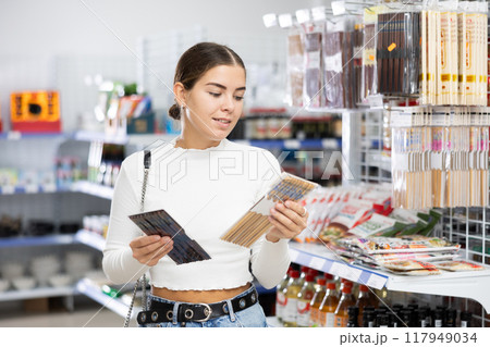 Girl customer chooses Chinese chopsticks in oriental goods department. 117949034