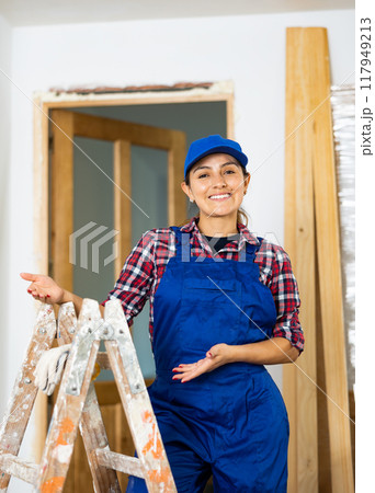 Young woman builder posing next to a stepladder in room being renovated Young woman builder posing next to a stepladder in room being renovated 117949213