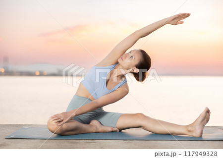 Near sea during sunset, girl performs variations of Janu Shirshasana Near sea during sunset, girl performs variations of Janu Shirshasana 117949328