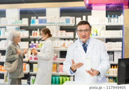 In pharmacy, male specialist holds and shows new effective remedy for moisturizing delicate skin In pharmacy, male specialist holds and shows new effective remedy for moisturizing delicate skin 117949405