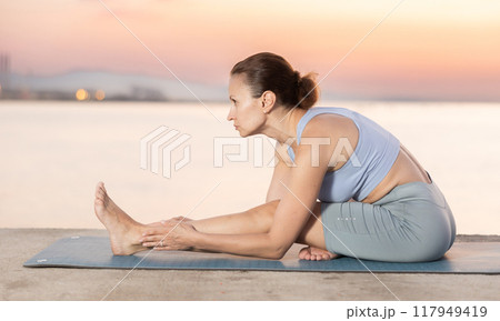 Portrait of young sporty woman making stretching legs and yoga pose on beach at morning Portrait of young sporty woman making stretching legs and yoga pose on beach at morning 117949419