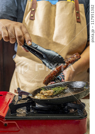 A person is cooking a sirloin steak in a pan with garlic and herbs A person is cooking a sirloin steak in a pan with garlic and herbs 117951382