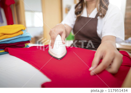 An Indonesian housewife is ironing a pile of clothes An Indonesian housewife is ironing a pile of clothes 117951434
