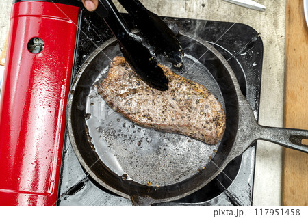 A person is cooking a picanha steak in a pan on a stove 117951458
