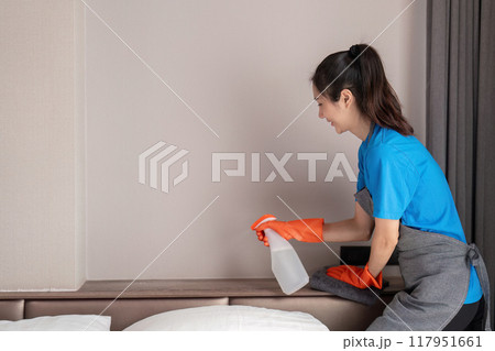 Housekeeper spraying cleaner on bedroom shelf for dusting Housekeeper spraying cleaner on bedroom shelf for dusting 117951661