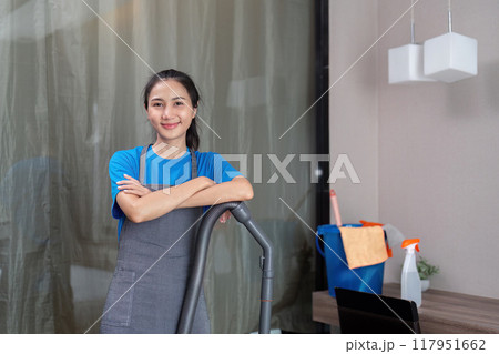 Asian female housekeeper smiling with vacuum in modern home Asian female housekeeper smiling with vacuum in modern home 117951662
