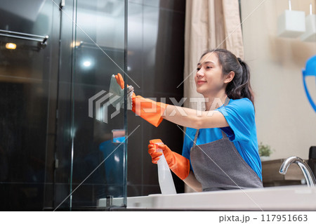 Housekeeper polishing bathroom glass with cleaning spray Housekeeper polishing bathroom glass with cleaning spray 117951663