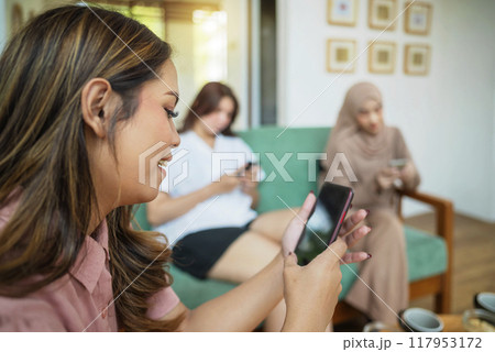 Three Indonesian woman sitting on a couch with her phone in her hand while video call Three Indonesian woman sitting on a couch with her phone in her hand while video call 117953172