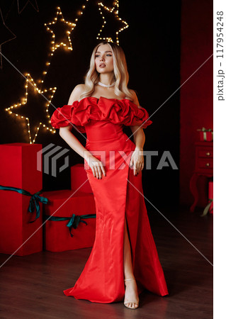 A woman in a red dress stands in front of a Christmas tree. Full length. A woman in a red dress stands in front of a Christmas tree. Full length. 117954248