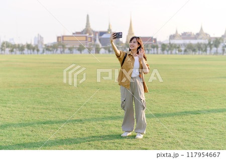 Traveler asian woman in her 30s take a livestream on smartphone while explores Wat Phra Kaew emerald Buddha. Share the wonders of Thai heritage through her journey. 117954667