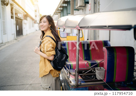 Young Asian woman backpack traveler standing a side of Tuk Tuk taxi on summer vacations at Bangkok, Thailand. Journey trip lifestyle, Asia summer tourism concept. Young Asian woman backpack traveler standing a side of Tuk Tuk taxi on summer vacations at Bangkok, Thailand. Journey trip lifestyle, Asia summer tourism concept. 117954710