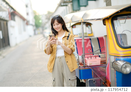 Young Asian woman backpack traveler standing a side of Tuk Tuk taxi on summer vacations at Bangkok, Thailand. Journey trip lifestyle, Asia summer tourism concept. Young Asian woman backpack traveler standing a side of Tuk Tuk taxi on summer vacations at Bangkok, Thailand. Journey trip lifestyle, Asia summer tourism concept. 117954712