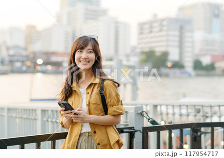 young Asian woman in 30s on a solo adventure. Technology in hand, she captures the essence of cultural exploration and joyful discovery. young Asian woman in 30s on a solo adventure. Technology in hand, she captures the essence of cultural exploration and joyful discovery. 117954717