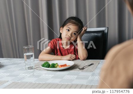 Mother is telling her cute kid eat useful vegetables but the child refuses to eat. Mother is telling her cute kid eat useful vegetables but the child refuses to eat. 117954776