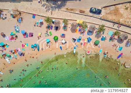 Sea beach with colorful umbrellas and relaxing people, aerial top view. Crowded sandy beach at high season. Tourists at summer holidays in Croatia 117954827
