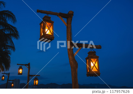 An old street lamp illuminating a dark street with palm trees 117957626