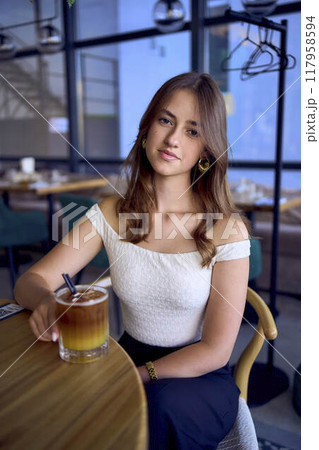 16-year-old teenage girl in old money style clothes drinks bumble coffee with an orange in a fancy restaurant 117958594