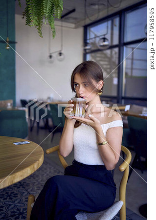 16-year-old teenage girl in old money style clothes drinks bumble coffee with an orange in a fancy restaurant 117958595