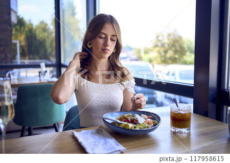 A 16-year-old teenage girl in old money style clothes is eating salad with coffee in a fancy restaurant A 16-year-old teenage girl in old money style clothes is eating salad with coffee in a fancy restaurant 117958615