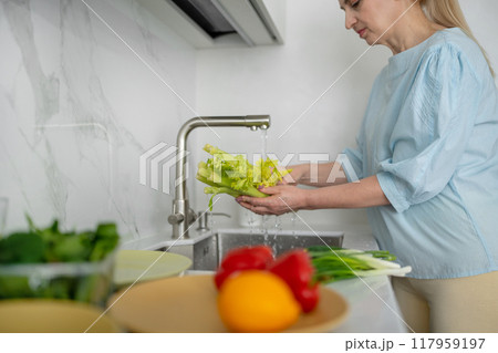 A woman is cleaning fresh vegetables in a modern kitchen to prepare a healthy meal 117959197