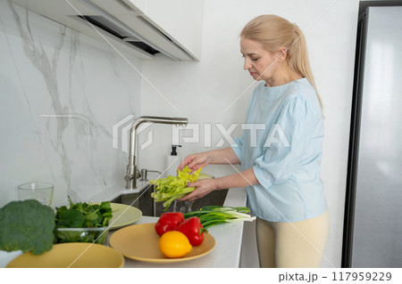 A woman is cleaning fresh vegetables in a modern kitchen to prepare a healthy meal A woman is cleaning fresh vegetables in a modern kitchen to prepare a healthy meal 117959229