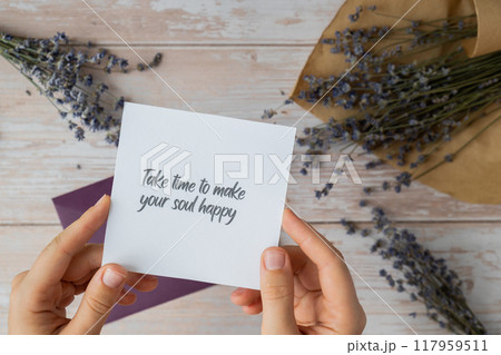 Female hands taking paper card note with text TAKE TIME TO MAKE YOUR SOUL HAPPY from violet envelope. Lavender flower. Top view, flat lay. Concept of mental spiritual health self care wellbeing Female hands taking paper card note with text TAKE TIME TO MAKE YOUR SOUL HAPPY from violet envelope. Lavender flower. Top view, flat lay. Concept of mental spiritual health self care wellbeing 117959511