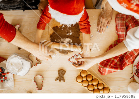 Top view and close up of small hands roll dough holding a rolling pin. Mother is holding a tree shaped metal cutter and father helps to hold the cutting board. Christmas cookies and holidays. Top view and close up of small hands roll dough holding a rolling pin. Mother is holding a tree shaped metal cutter and father helps to hold the cutting board. Christmas cookies and holidays. 117959598