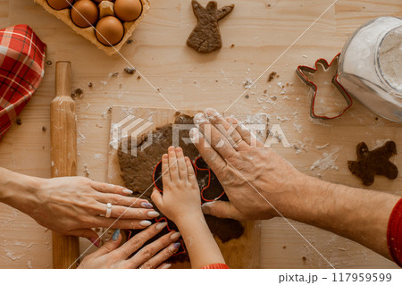 The family cooks homemade ginger cookies for Christmas. Moms, father's hands and son's hands on the dough against the background of the table. Top View The family cooks homemade ginger cookies for Christmas. Moms, father's hands and son's hands on the dough against the background of the table. Top View 117959599