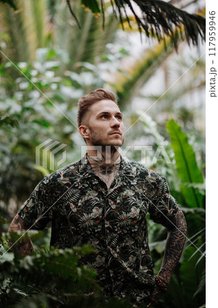 Handsome man with tattoo standing in botanical garden, in the middle of lush green foliage. Handsome man with tattoo standing in botanical garden, in the middle of lush green foliage. 117959946