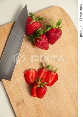 The strawberries are cut into slices. they lie on a wooden board and next to the knife The strawberries are cut into slices. they lie on a wooden board and next to the knife 117961605