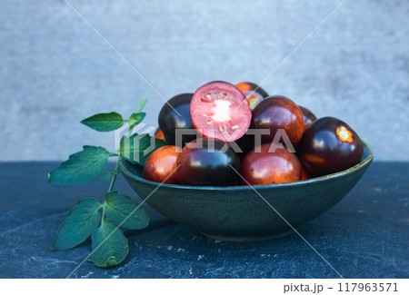 Black tomatoes of Indigo Rose in a bowl on the stone table. 117963571