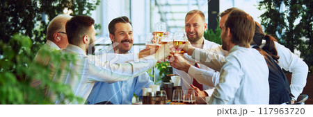 Cheers to successful project. Group of colleagues, business people, men clinking beer glasses, sitting at outdoor bar and celebrating good work 117963720