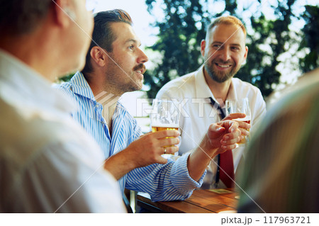 Cheerful people, businessmen, colleagues sitting at outdoor bar, restaurant, drinking beer, talking, discussing successful projects and partnership Cheerful people, businessmen, colleagues sitting at outdoor bar, restaurant, drinking beer, talking, discussing successful projects and partnership 117963721