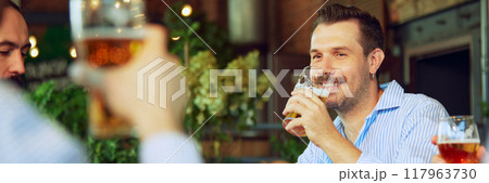 Smiling positive man in formal wear drinking beer with joy and fun, meeting with colleagues after work and relaxing. Smiling positive man in formal wear drinking beer with joy and fun, meeting with colleagues after work and relaxing. 117963730