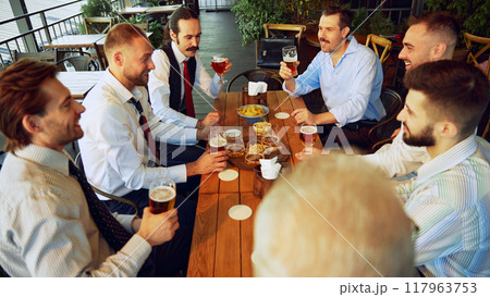 Colleagues, businessmen relaxing at the bar with beers, balancing work with bit of fun. Celebrating well-coordinated teamwork and success 117963753