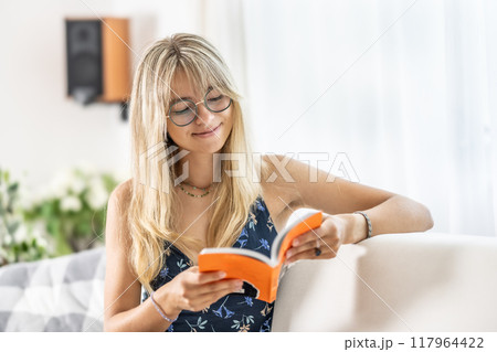A young lady is reading a book and wearing prescription glasses. 117964422
