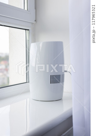 Modern air humidifier on a windowsill behind the curtains. 117965321