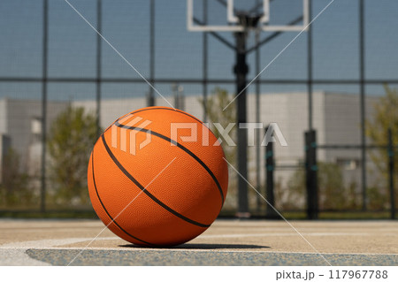 Basketball orange ball lies at outdoor public basketball court. Sports gear without people. Template, sport background. Close up. 117967788