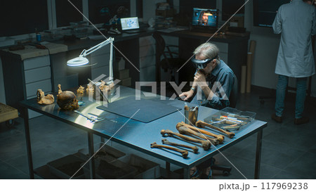 Mature archaeologist in AR headset conducts historical research on fossil bones remains 117969238