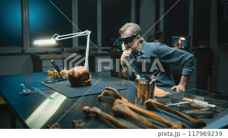 Mature archaeologist in VR headset examines fossil skull 117969239