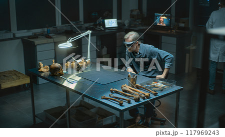 Mature archaeologist in AR headset conducts historical research on fossil bones remains 117969243