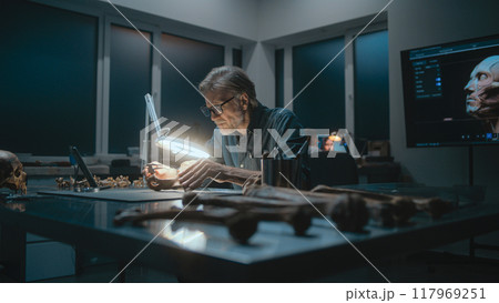 Archaeologist takes measurements of fossil bone under lamp, uses tablet computer Archaeologist takes measurements of fossil bone under lamp, uses tablet computer 117969251