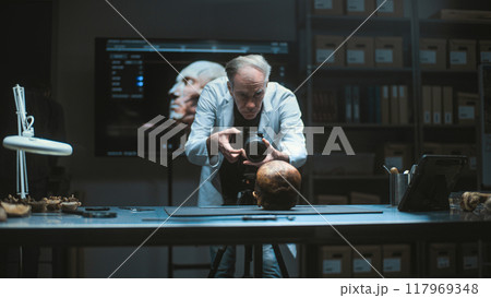 Senior archaeologist takes photo of prehistoric human skull with professional camera Senior archaeologist takes photo of prehistoric human skull with professional camera 117969348