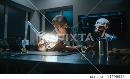 Archaeologist takes measurements of fossil bone under lamp, uses tablet computer 117969384