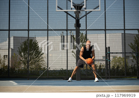 Sporty adult man playing with orange basketball ball on sports court at courtyard. Street style. Team sport. Fun exercise. Basketball coach. Game moment. 117969919