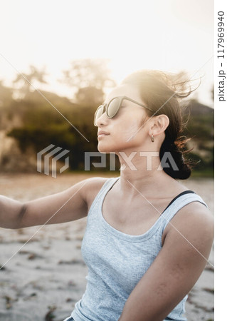 風が強い砂浜でサングラスをかけている若い日本人女性 117969940